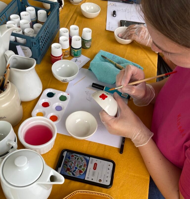 Vaiselle sur une table, peinture et une personne entrain de décorer une tasse