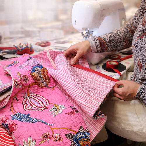 Participant à un atelier couture en train de confectionner un gilet en tissu matelassé rose, installé devant une machine à coudre dans une ambiance chaleureuse et créative.